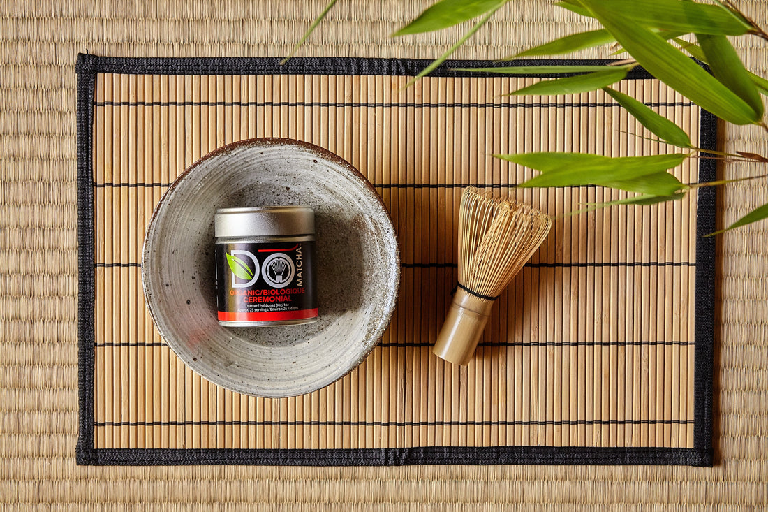 A bowl with a container of organic ceremonial matcha and a whisk on a bamboo mat.