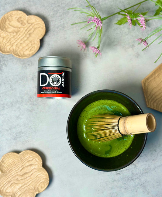 A bowl of organic ceremonial matcha green tea with a wooden whisk and a container with a bamboo whisk.