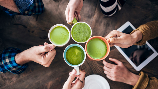 A group of people holding cups of liquid pure matcha green tea powder.